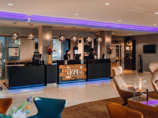 A hotel reception area with a modern design, featuring a reception desk, seating area, and a large vase with flowers.
