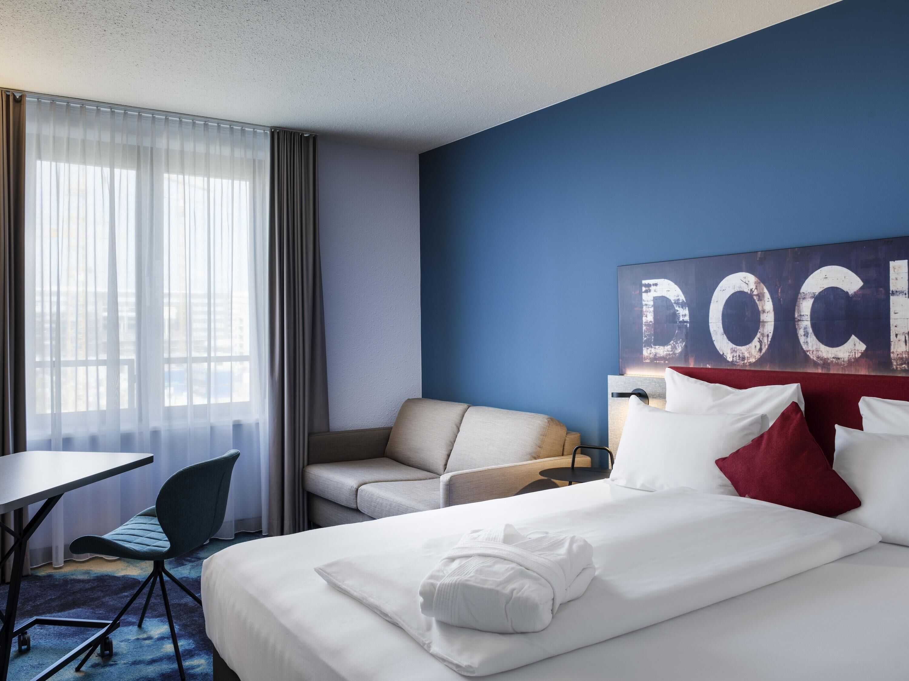Ein Hotelzimmer mit Bett, Schreibtisch, Sessel und einer großen Wandkunst.