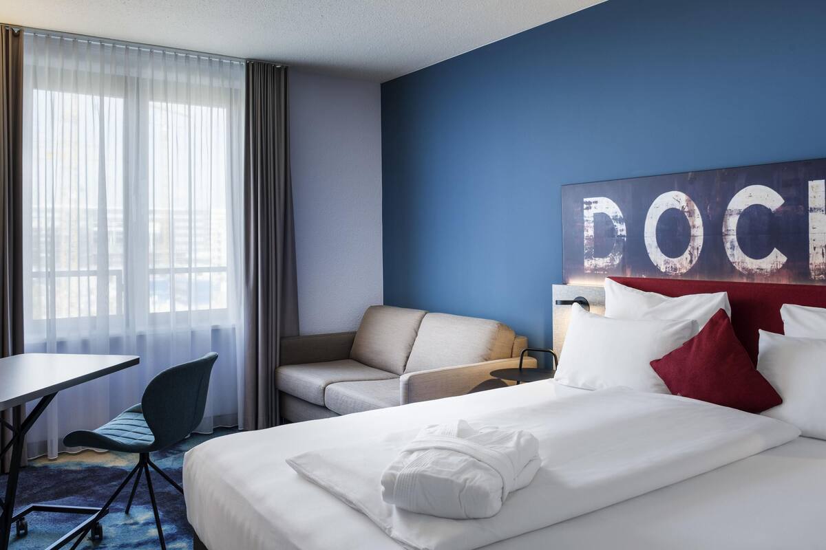 Ein Hotelzimmer mit Bett, Schreibtisch, Sessel und einer großen Wandkunst.