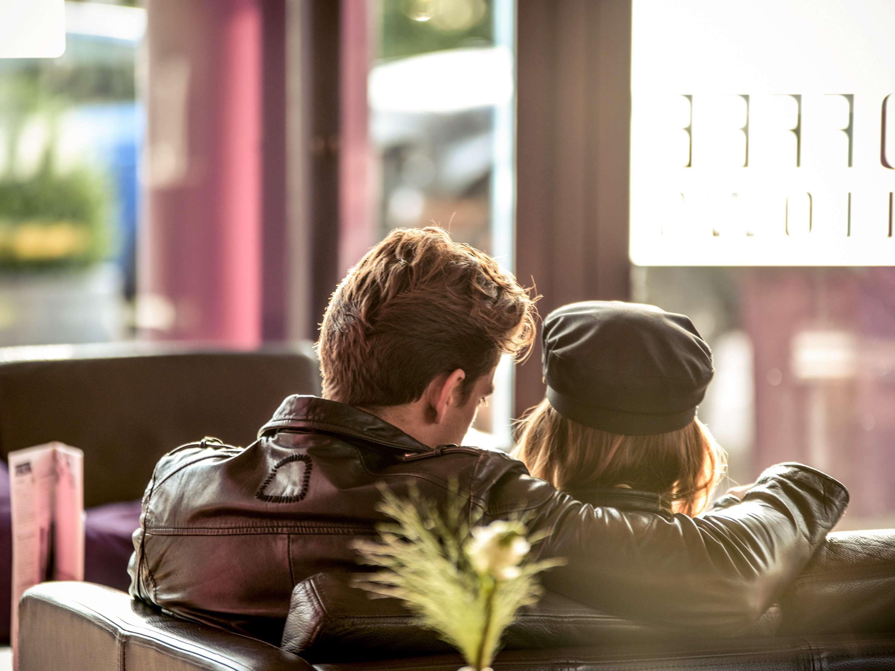 A couple sitting on a leather couch facing a window with a view of a street.