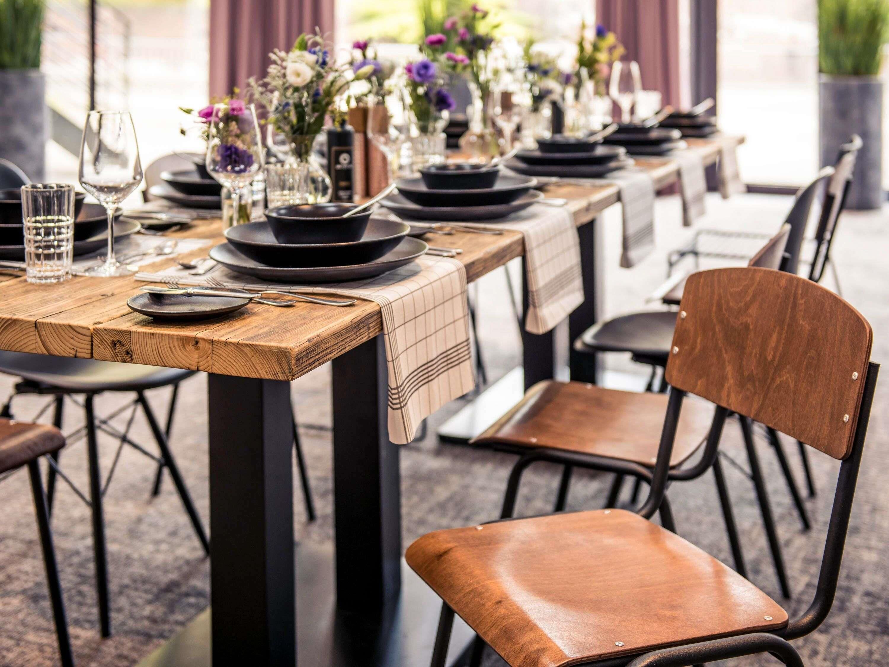 A dining table set with plates, glasses, and cutlery, chairs, and a vase with flowers.