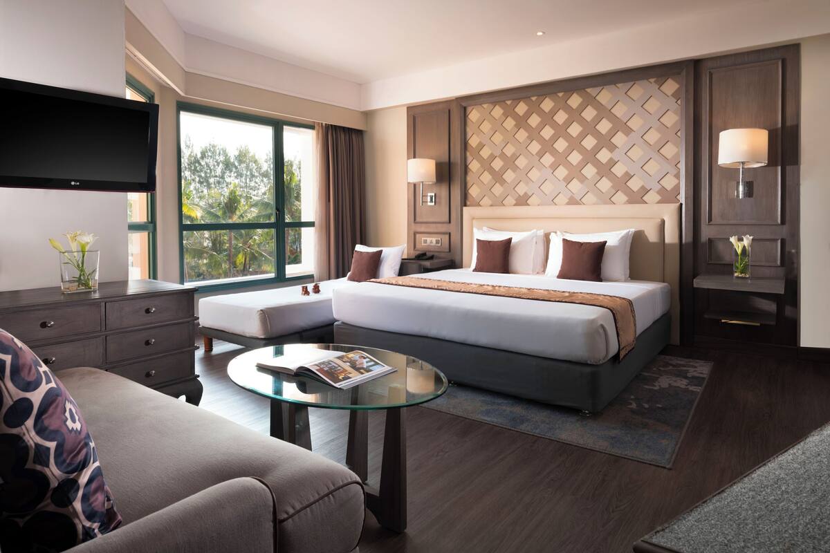 A modern hotel room with a large bed, a glass coffee table, a sofa, and a TV.