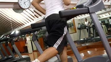 A person running on a treadmill in a gym with a clock on the wall.