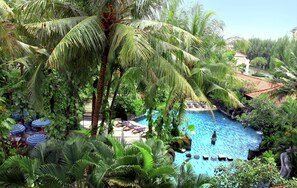 Una piscina rodeada de exuberantes palmeras y follaje tropical, con sillones de descanso y sombrillas.