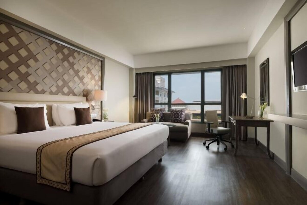 Habitación de hotel con una cama grande, un escritorio, una silla y vistas a un edificio a través de la ventana.