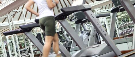 A woman running on a treadmill in a gym with various exercise equipment in the background.