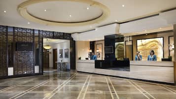 A hotel lobby with a reception desk, a decorative ceiling, and a patterned floor.