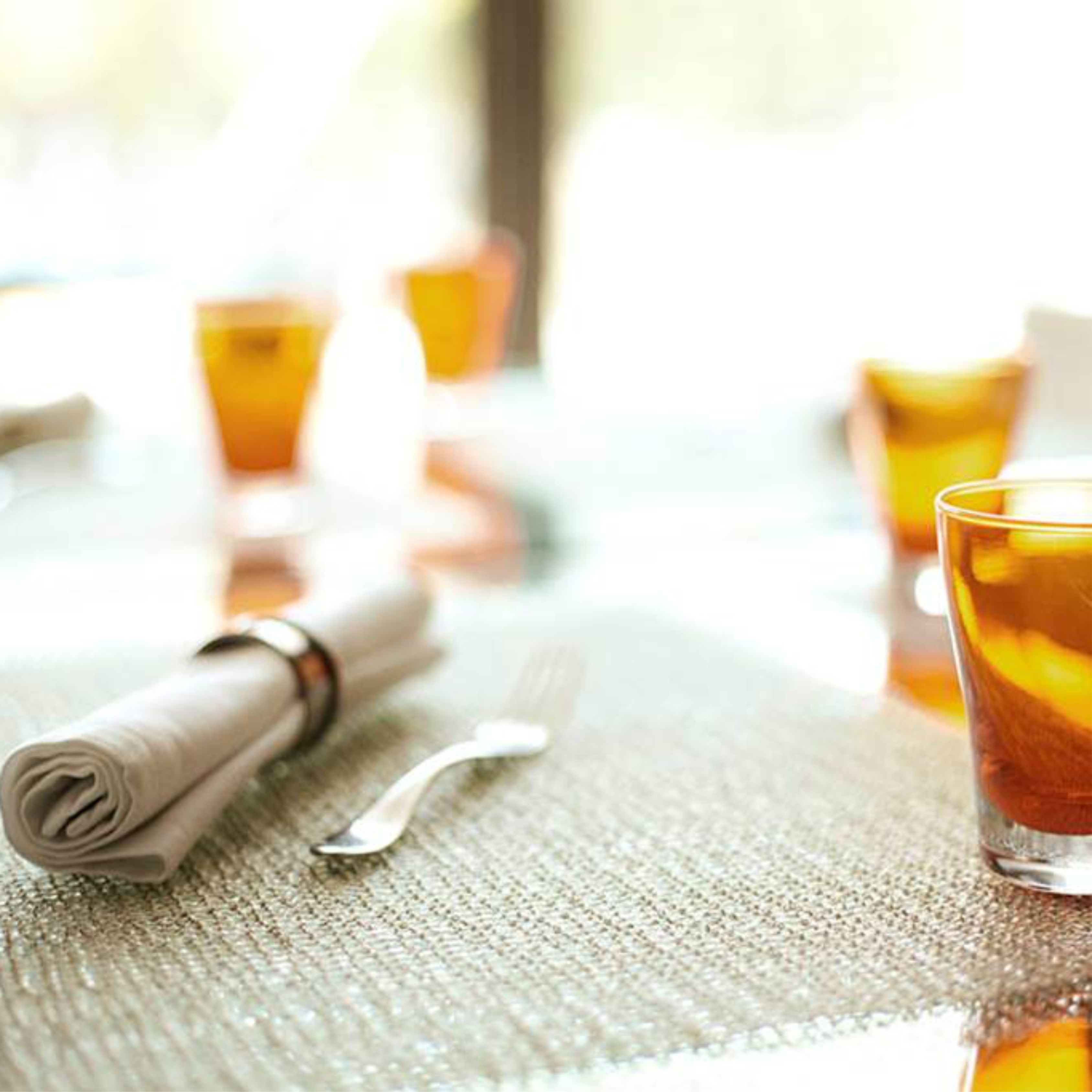 A table with a folded napkin, a fork, and a glass with a beverage.