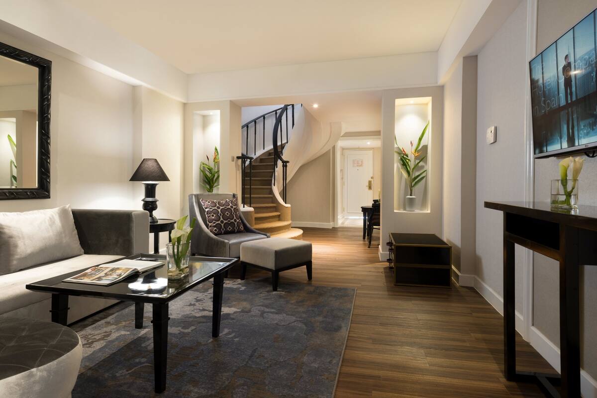 A modern living room with a sofa, armchair, coffee table, and a staircase leading to another level.