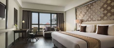 A hotel room with a large bed, a desk, a chair, and a view of the city.