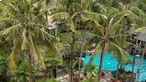 A tropical resort with a central pool, palm trees, and outdoor seating areas.