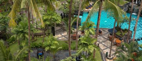 Un resort tropical con piscina central, palmeras y zonas de estar al aire libre.