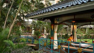 A covered outdoor area with a tiled roof, a blue railing, and a person sitting on a bench.