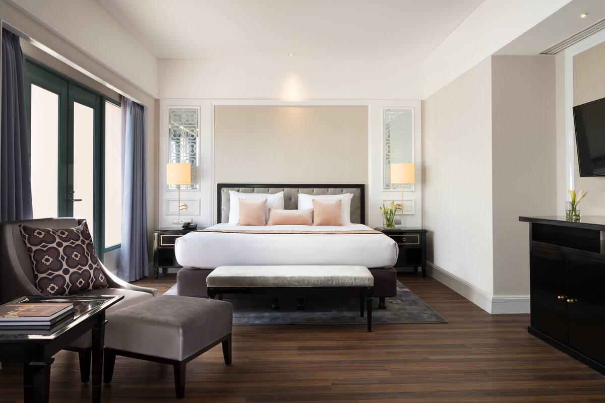 A modern hotel room with a large bed, bedside lamps, a television, a desk, and a chair.