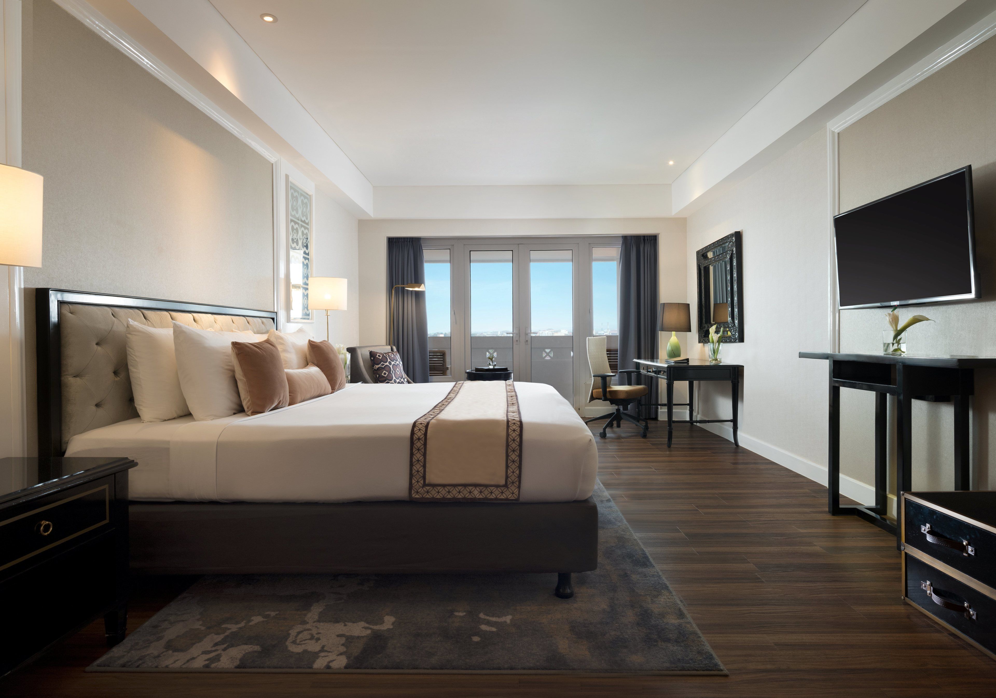 Habitación de hotel con una cama grande, un escritorio, una silla, un televisor y una ventana con cortinas.