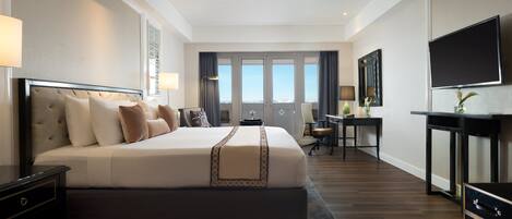 Habitación de hotel con una cama grande, un escritorio, una silla, un televisor y una ventana con cortinas.
