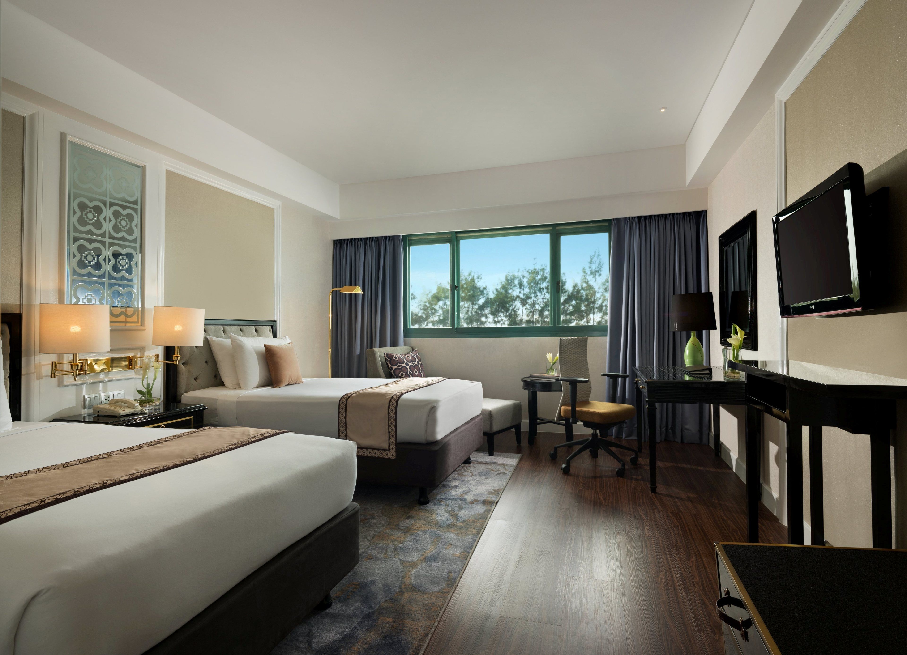 A hotel room with two beds, a desk, a chair, a television, and a window with curtains.