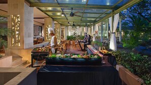 An indoor dining area with a glass ceiling, tables, and chairs, surrounded by plants and a view of the outdoors.
