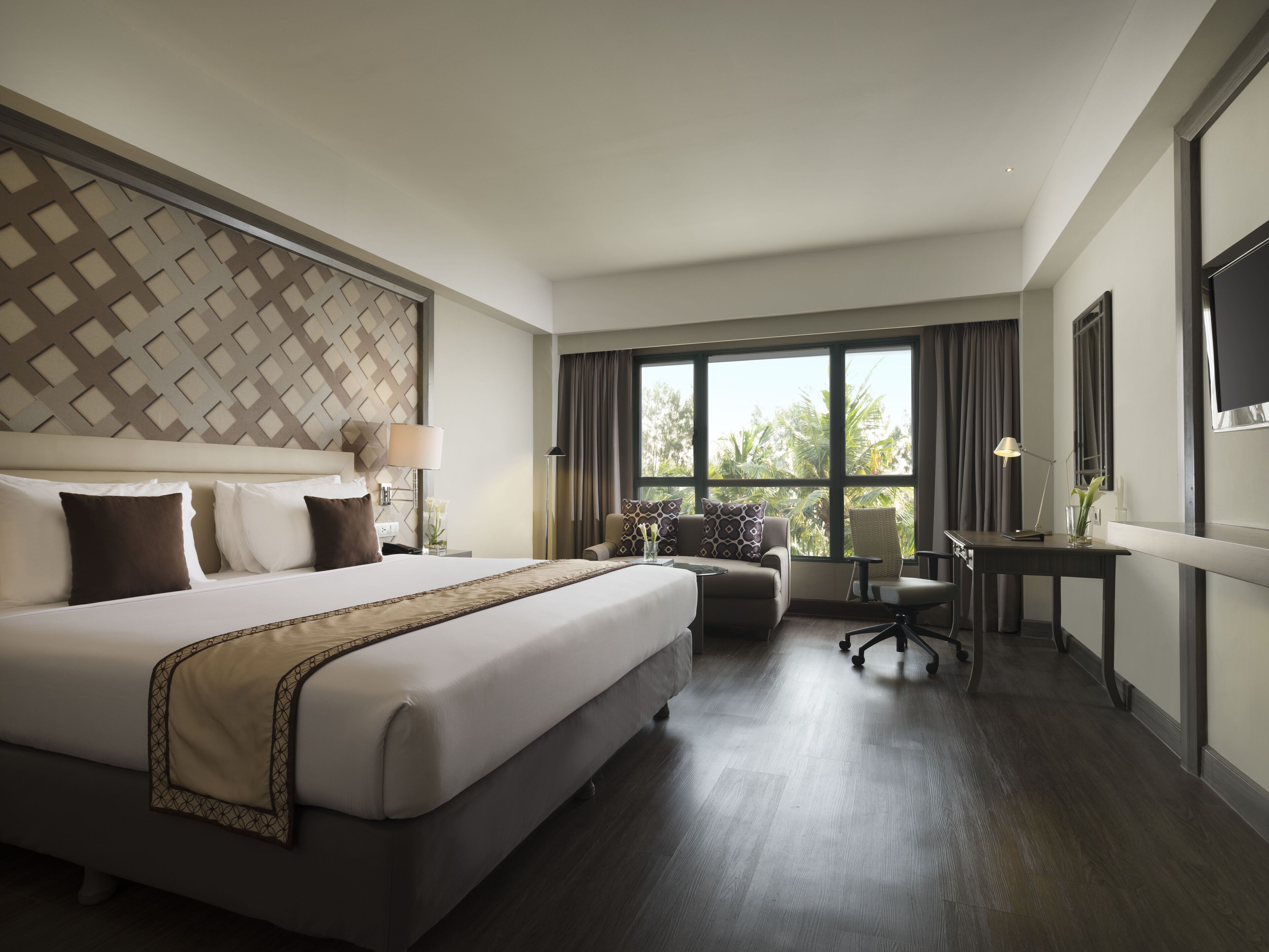 A modern hotel room with a large bed, a desk, and a view of the outdoors.
