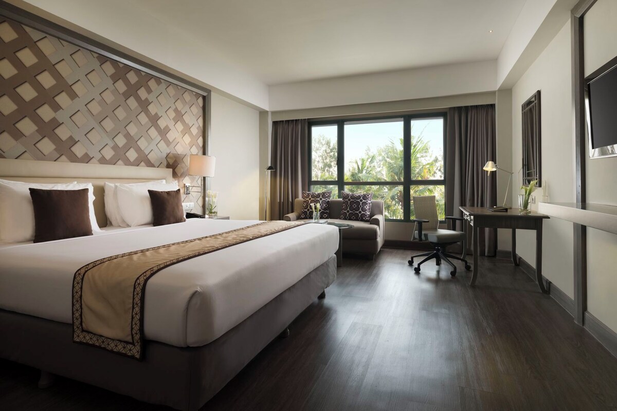 A hotel room with a large bed, a desk, a chair, and a TV.
