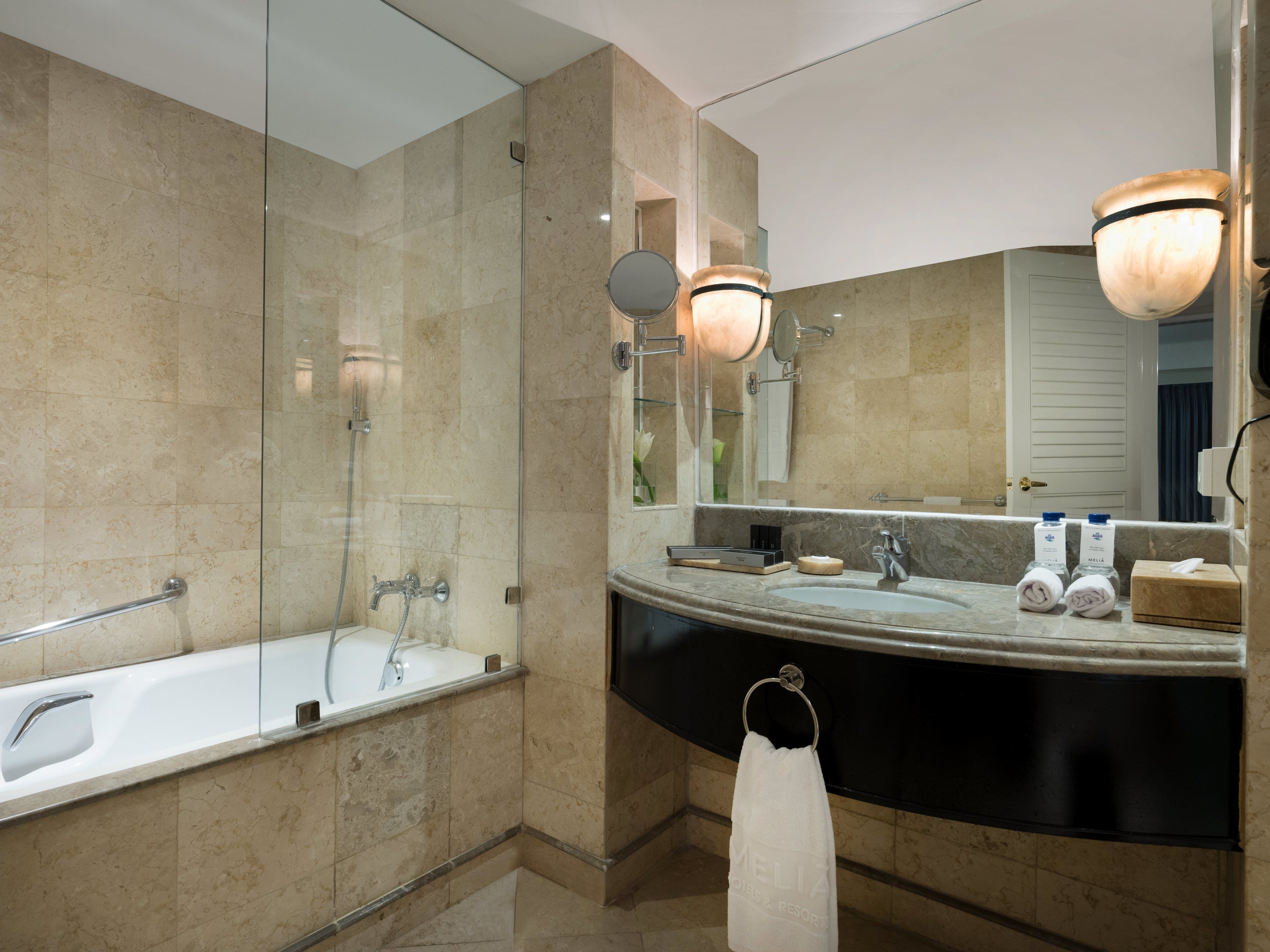 Un baño moderno con ducha envuelta en vidrio, un espejo grande y un tocador con encimera negra.