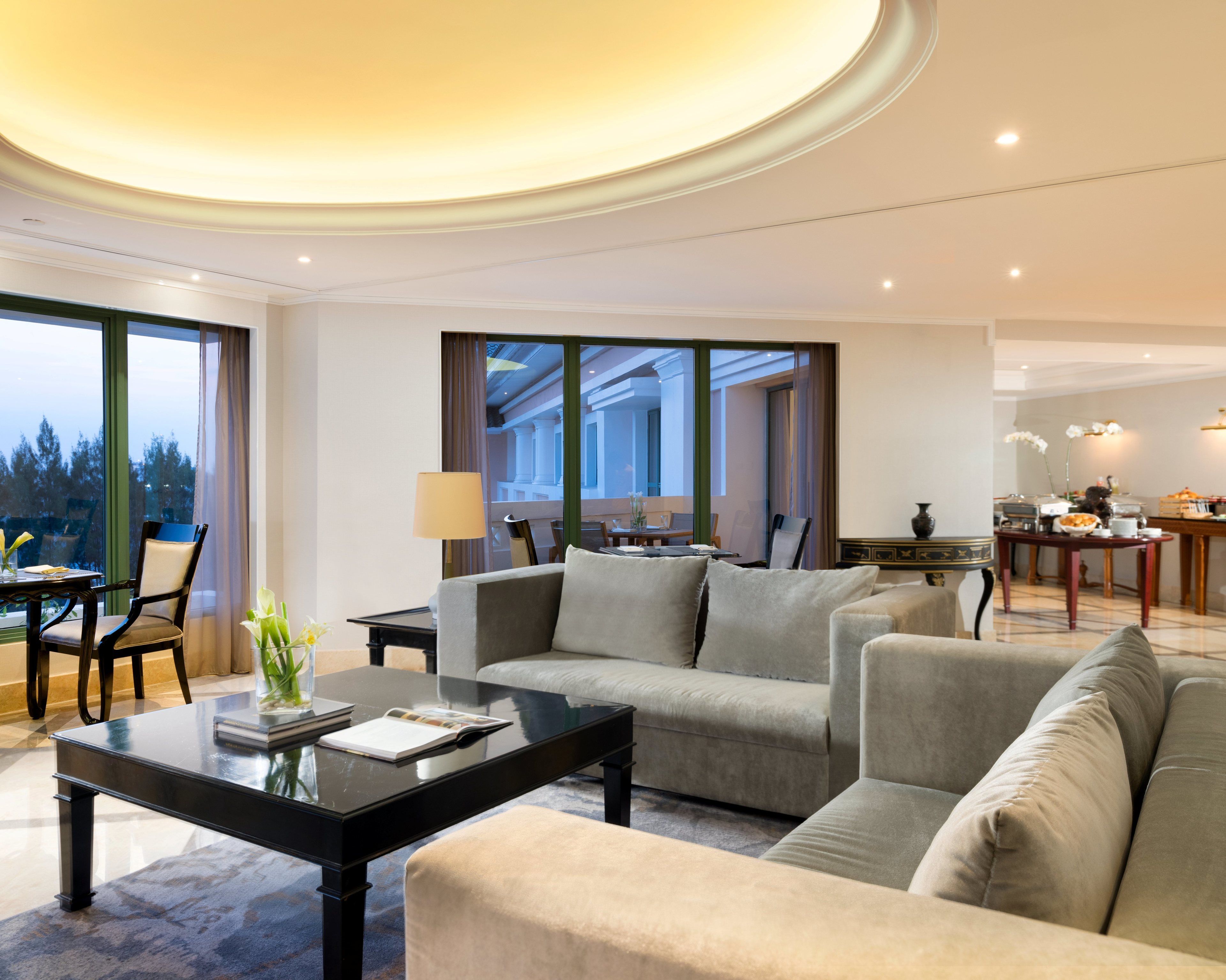A modern hotel room with a living area featuring a sofa set, a dining table, and a view of the outdoors.