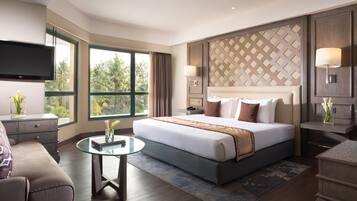 A modern hotel room with a large bed, a flat-screen TV, a desk, and a view of palm trees.