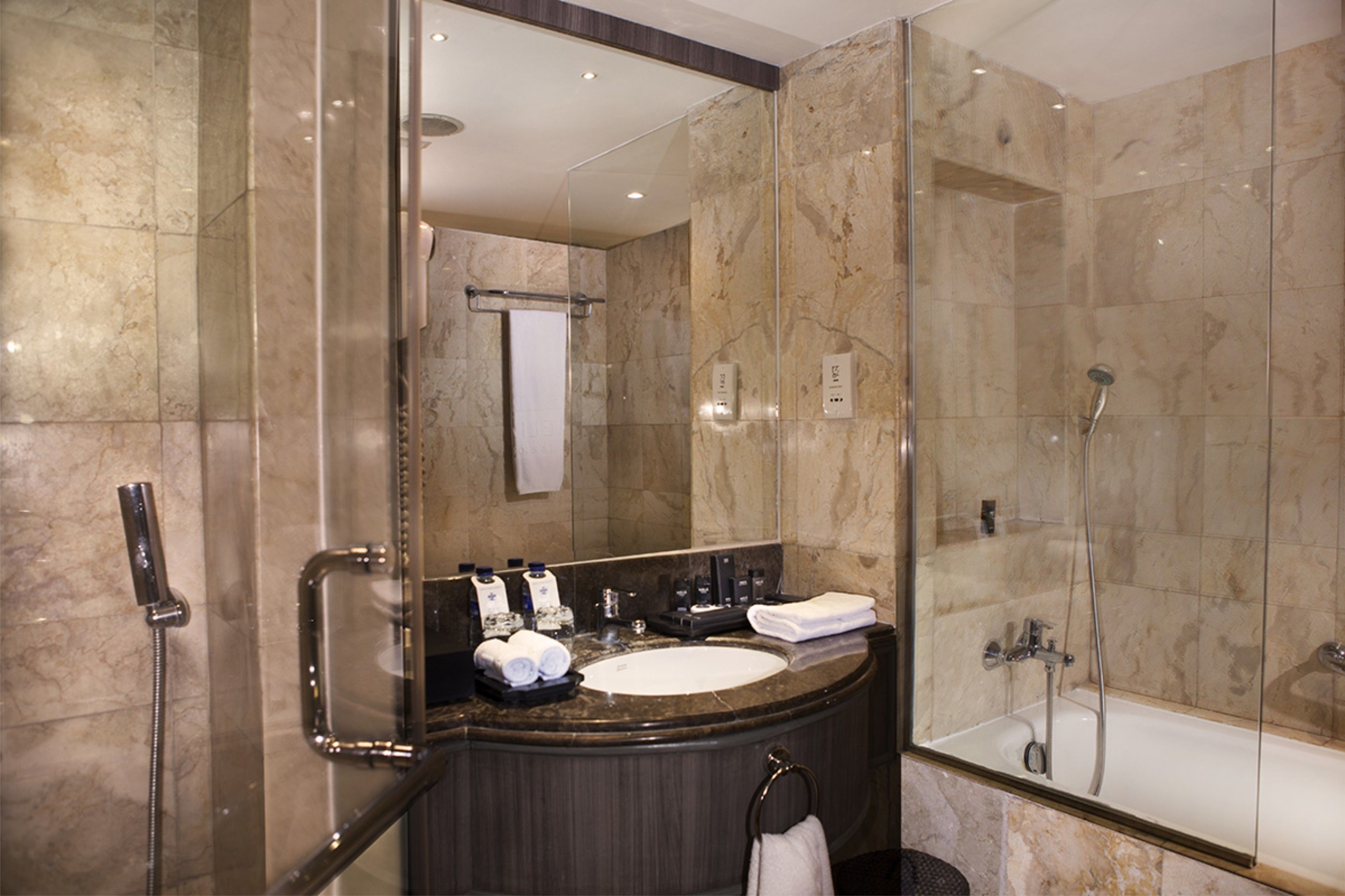 A modern bathroom with a marble sink, a glass-enclosed shower, and a large mirror.