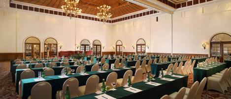 A large conference room with long tables, chairs, and chandeliers.