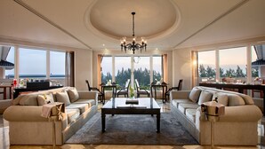 Un salón espacioso con una mesa de centro grande, dos sofás y un comedor con sillas. Amplias ventanas ofrecen vistas al exterior.