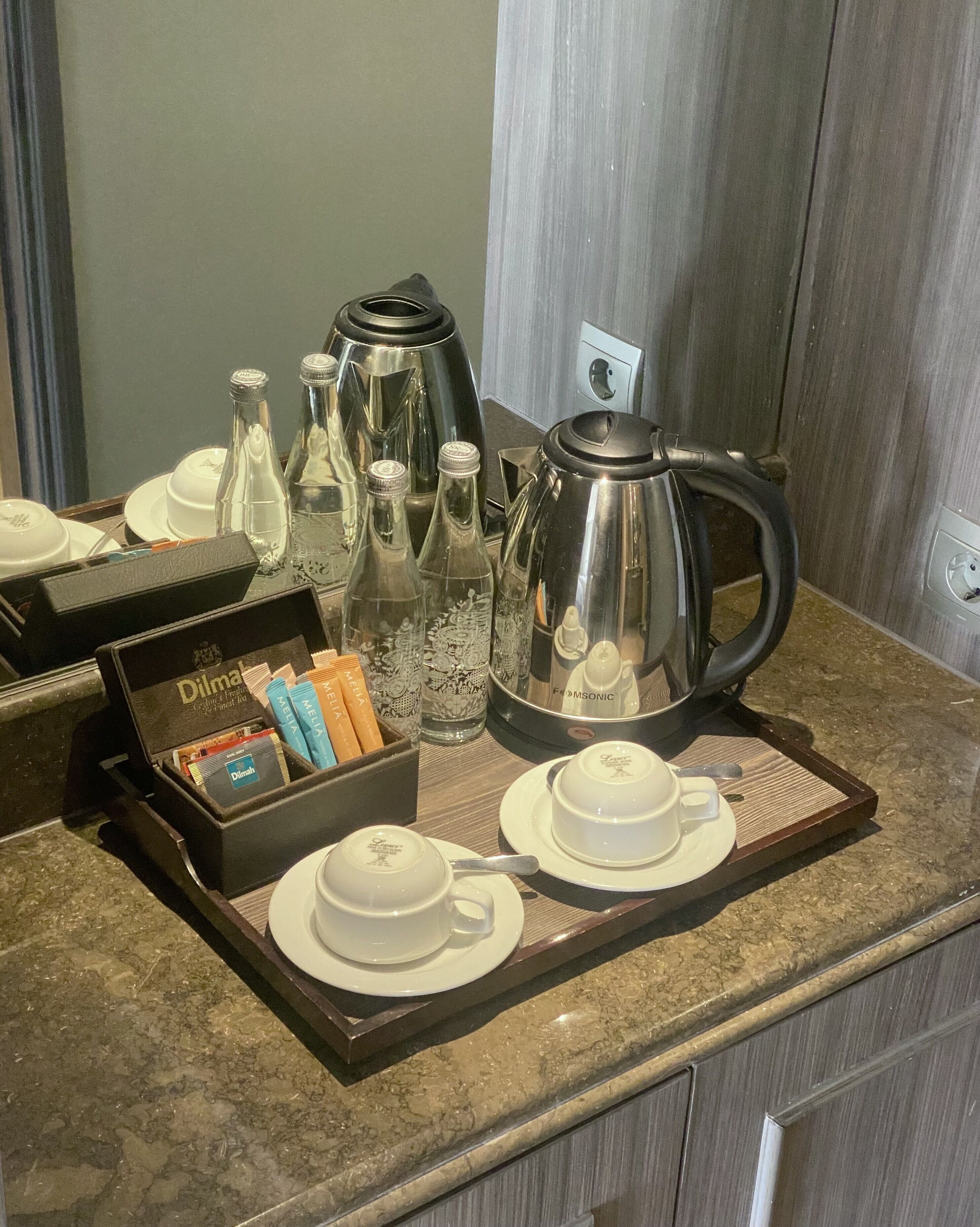 A breakfast tray with coffee pot, cups, and tea service on a marble countertop.