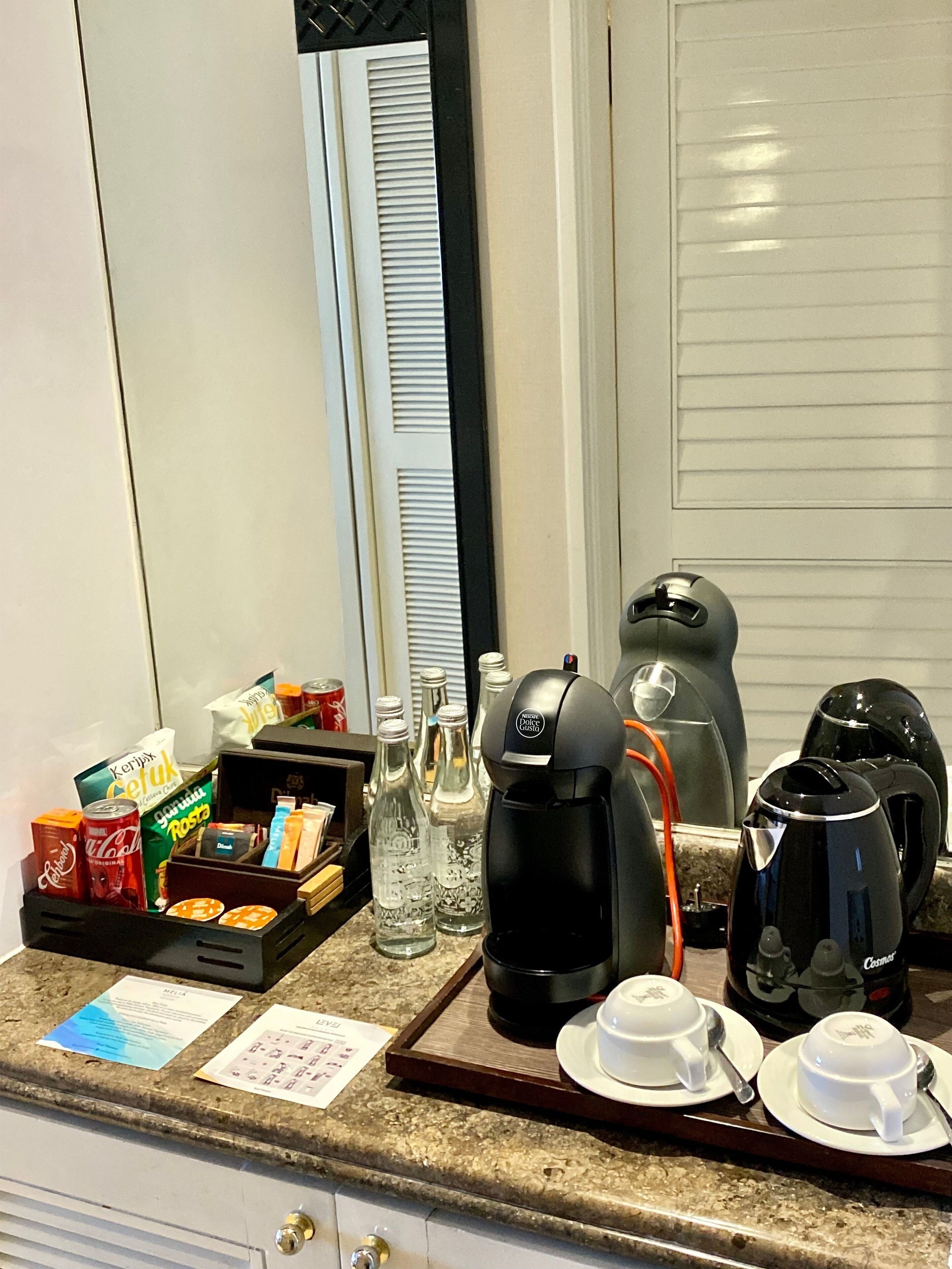 A hotel room's breakfast setup with a coffee maker, cups, and condiments on the counter.