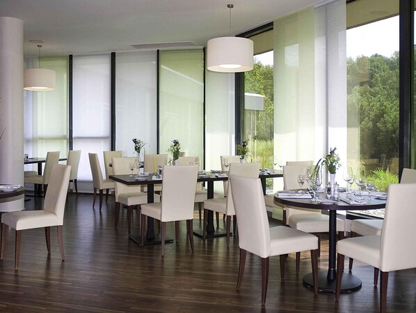 Un comedor moderno con ventanas amplias, suelo de madera y sillas blancas.