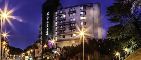 Un edificio de hotel con varios pisos, un letrero llamativo y una calle bien iluminada al frente.