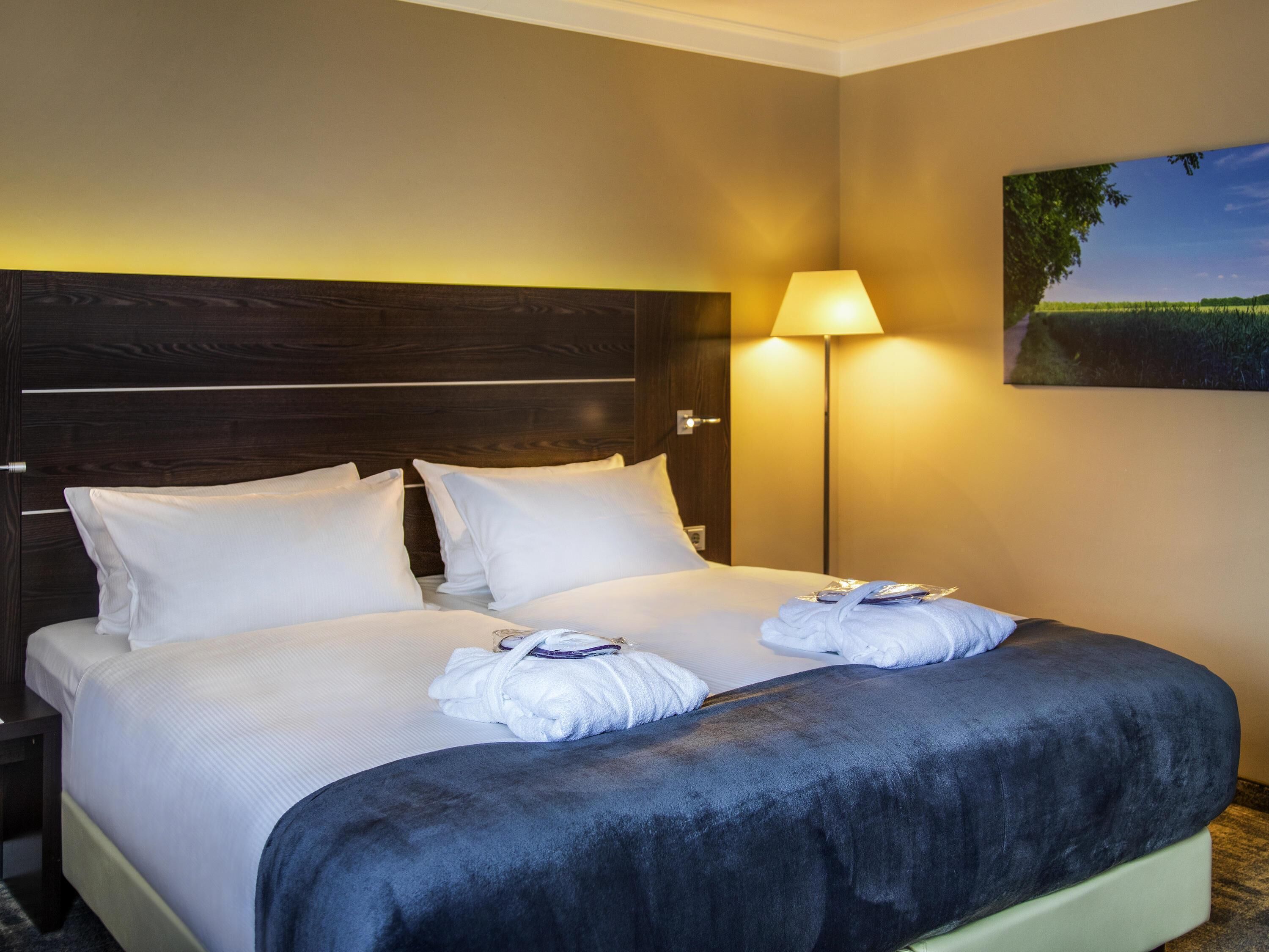 A hotel room with a large bed, a nightstand, a lamp, and a painting on the wall.