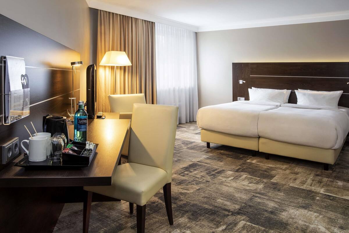 A hotel room with a bed, a desk with a lamp, a coffee maker, and a minibar.