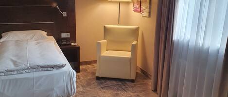 A hotel room with a bed, a chair, a lamp, and a painting on the wall.
