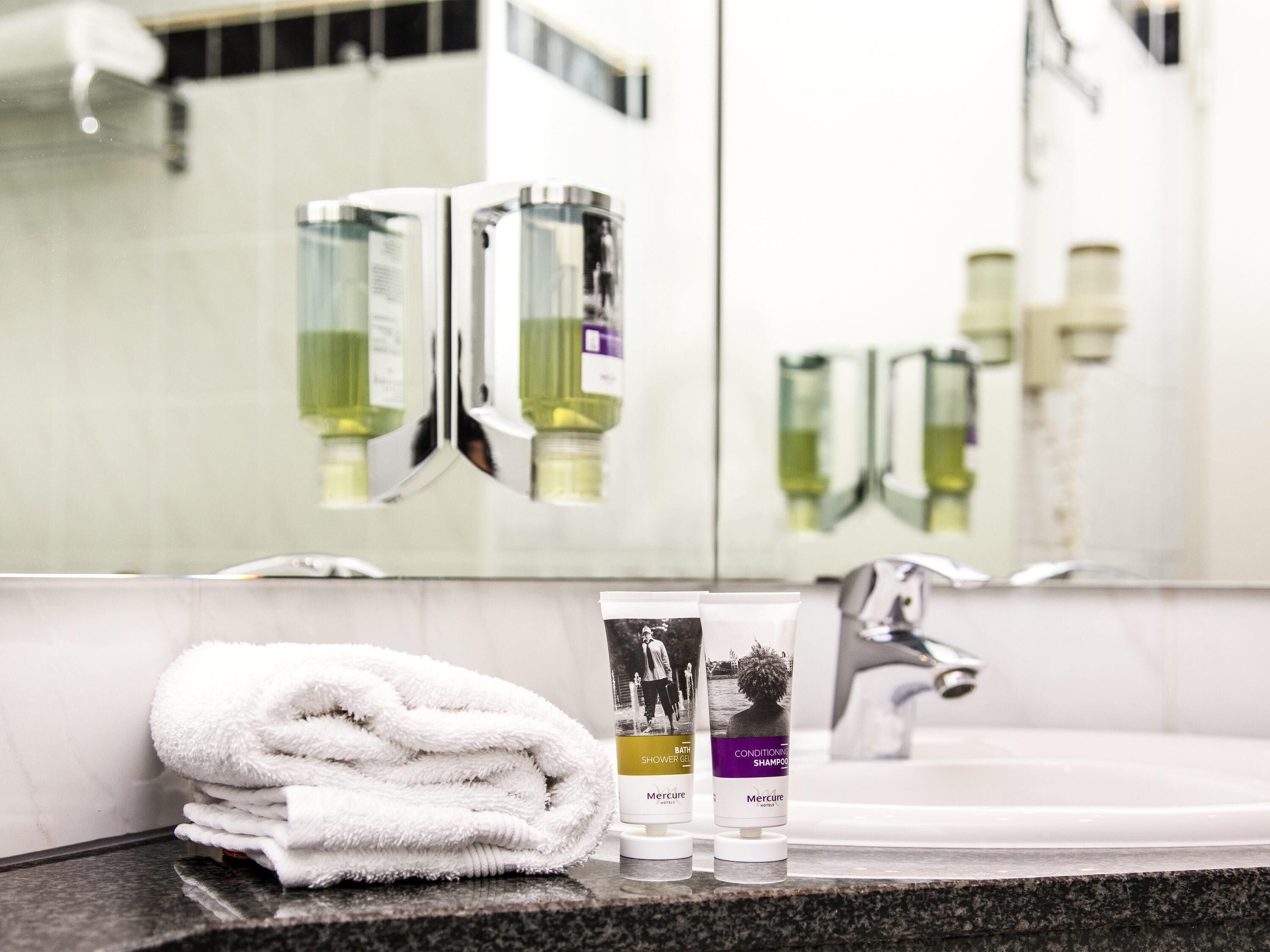 A bathroom with a sink, two bottles of shampoo, and a folded towel on the counter.