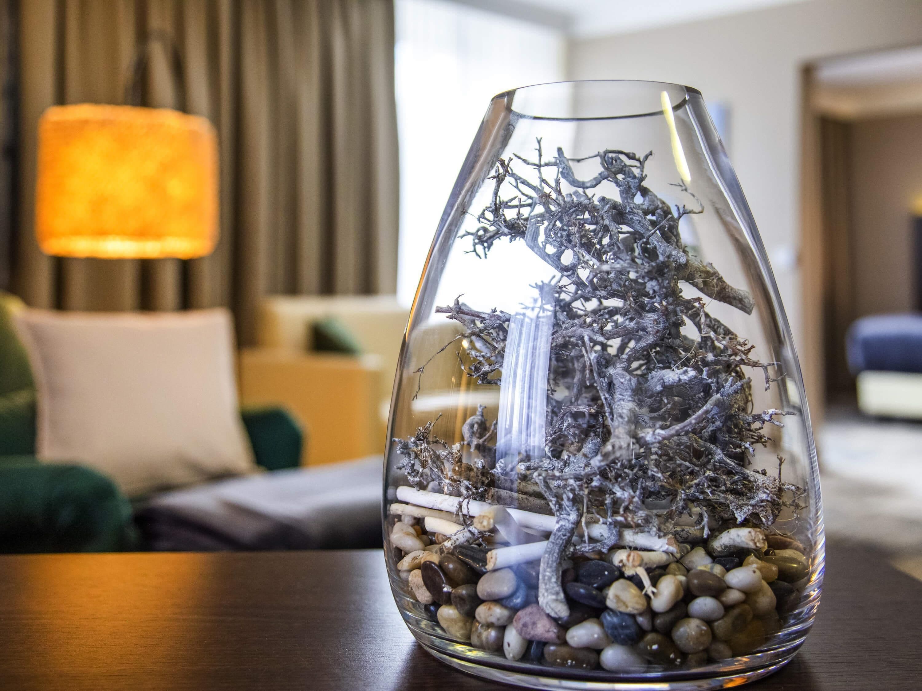 Un jarrón de cristal transparente con una rama y guijarros sobre una mesa de madera.