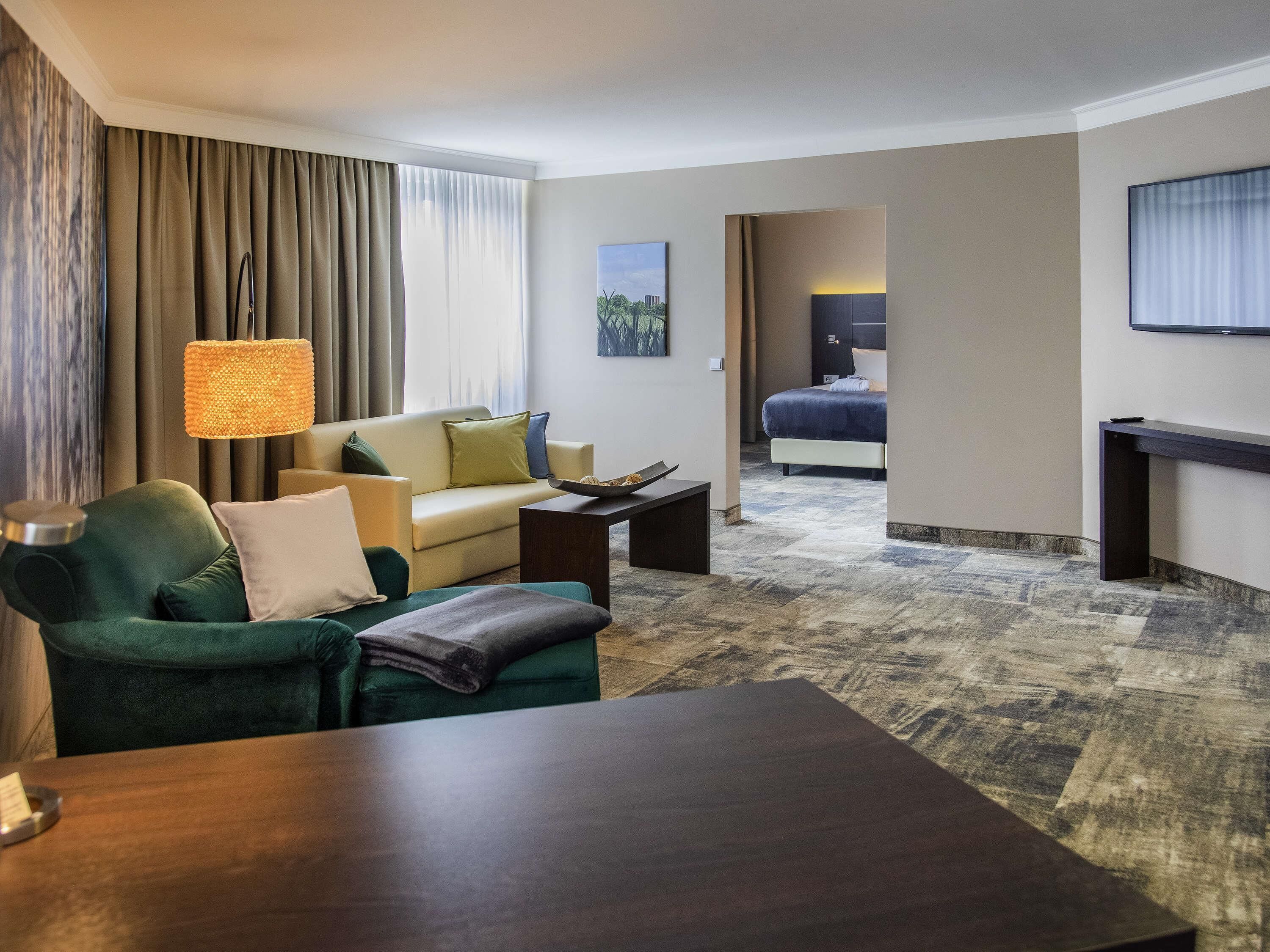 A hotel room with a sofa, a coffee table, a bed, a TV, and a lamp.