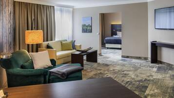 Una habitación de hotel con un sofá, una mesa de centro, una cama, un televisor y una lámpara.