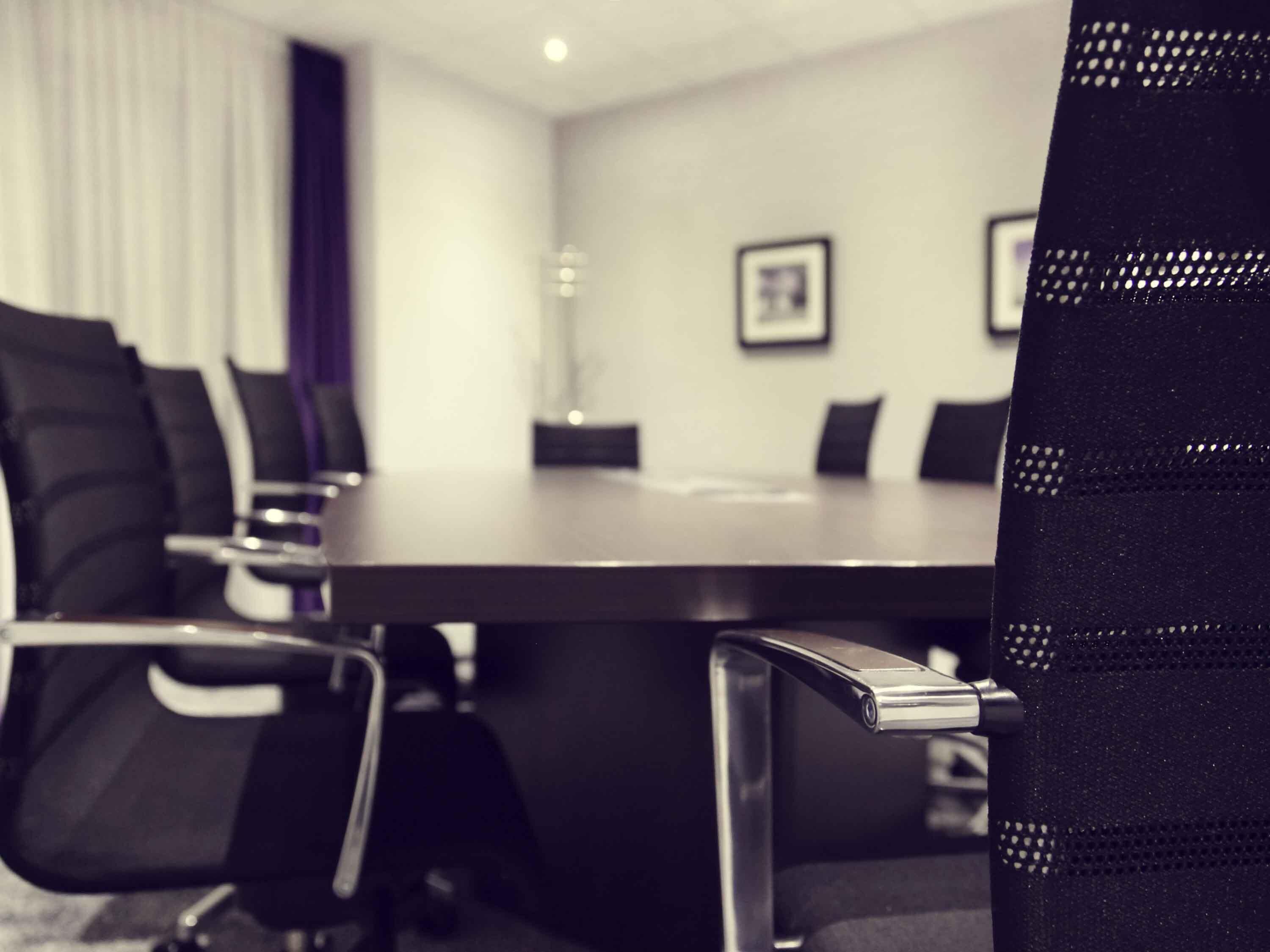 Un salón de conferencias con una larga mesa, sillas negras y una pizarra en la pared.