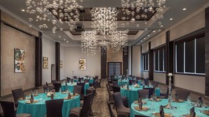 Une salle de conférence avec des tables rondes, des nappes de couleur turquoise et des chaises sombres.