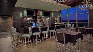 Un bar moderne doté d’un comptoir élevé, de nombreux espaces pour s’asseoir et offrant une vue sur le paysage urbain au crépuscule.
