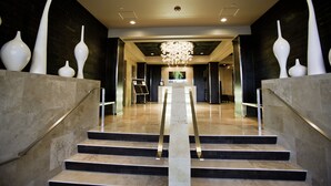 Un magnifique escalier, surmonté d’un lustre moderne, mène à un hall d’entrée doté d’un mur sombre et d’un tableau encadré.