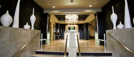 A grand staircase with a modern chandelier, leading to a lobby area with a dark wall and a framed picture on the wall.