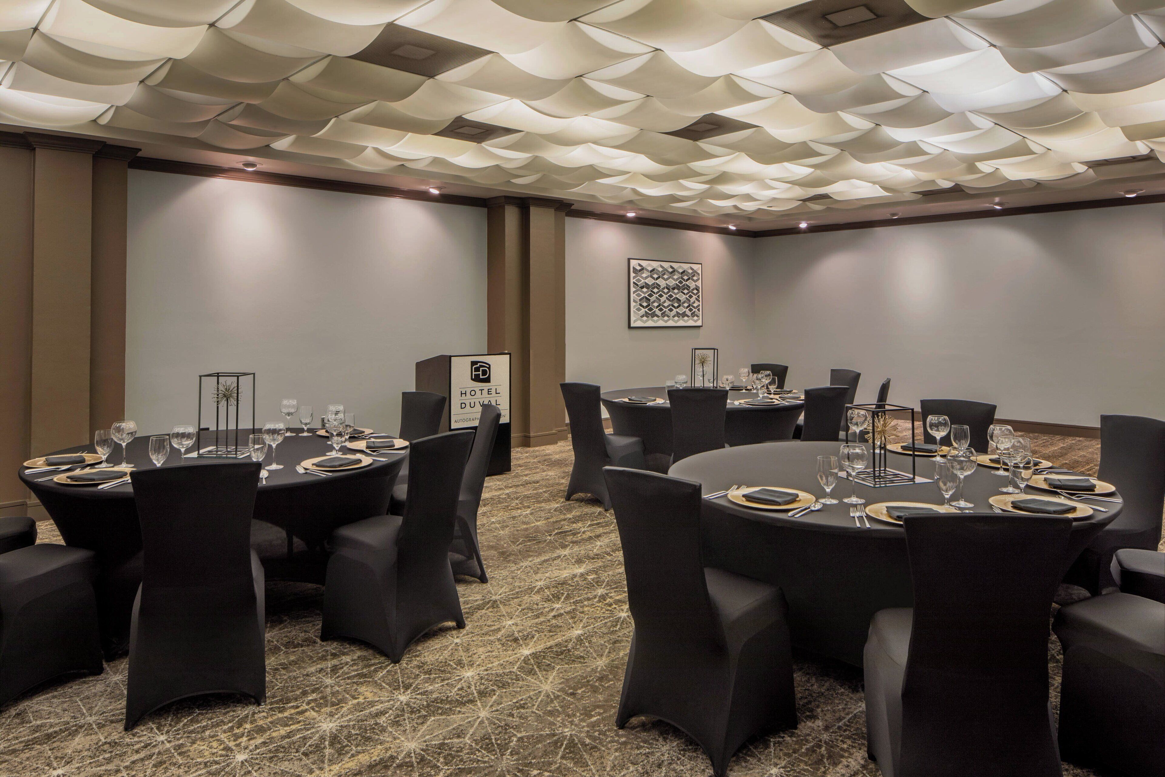 Une salle de conférence avec des tables rondes, des chaises noires et un tapis à motifs.