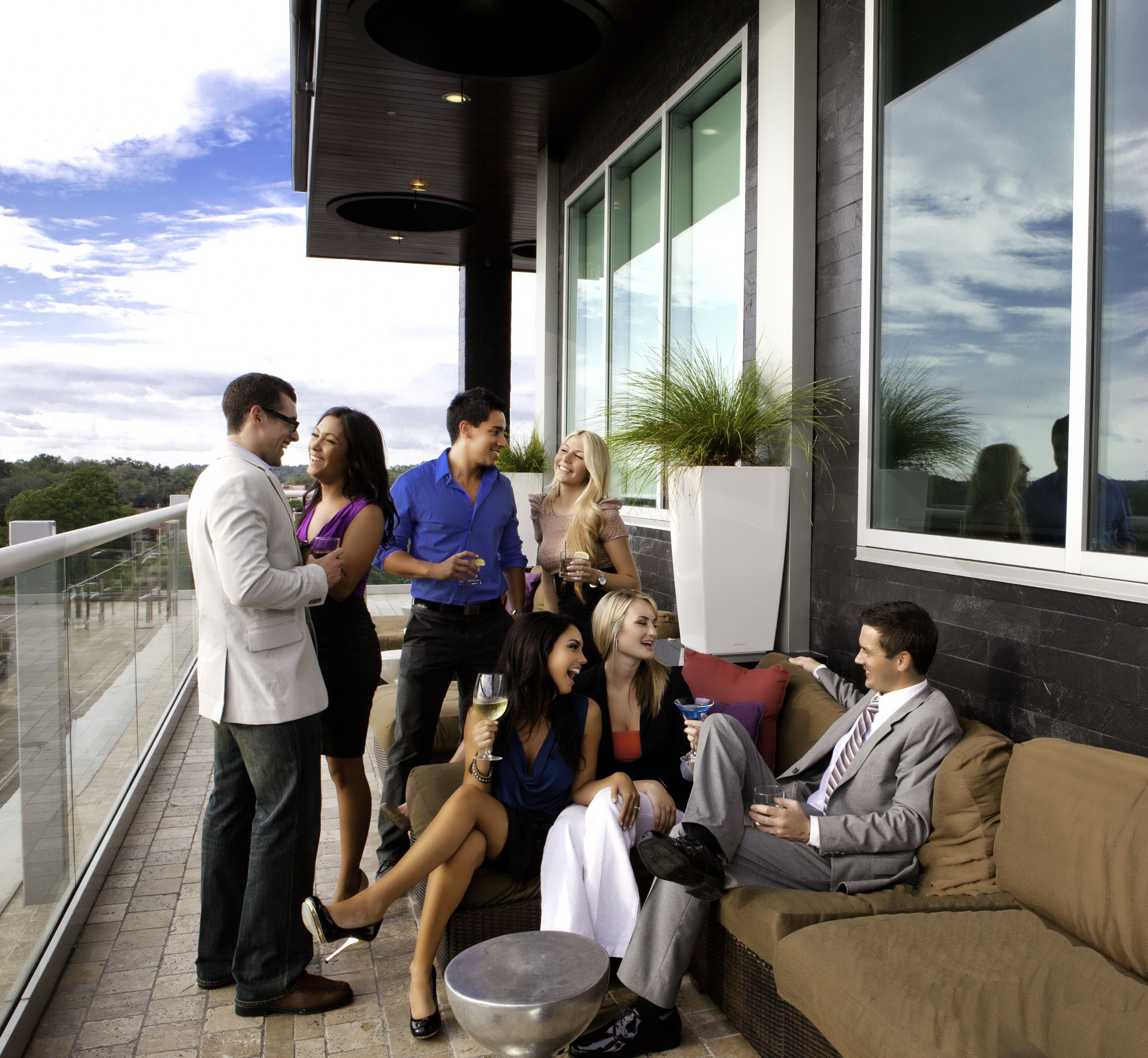 A group of people socializing on a balcony with a view of the sky and trees.