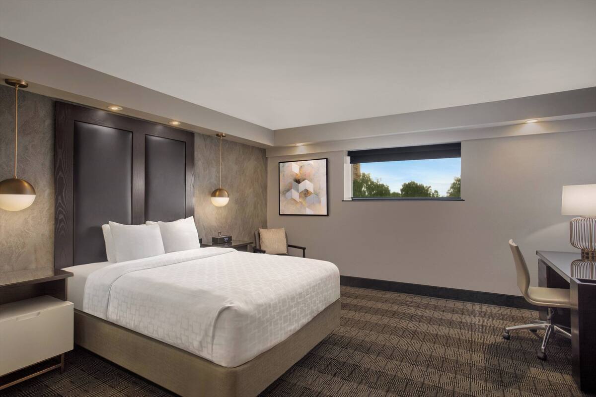 Habitación de hotel con una cama grande, un escritorio, una silla, una ventana con vistas y obras de arte colgadas en la pared.