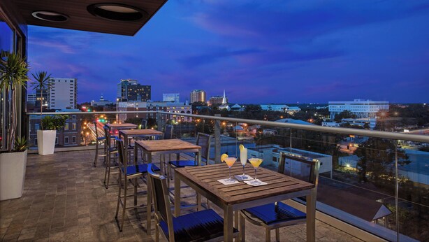 Une terrasse sur le toit, aménagée avec des tables et des chaises, offrant une vue sur la ville au crépuscule.